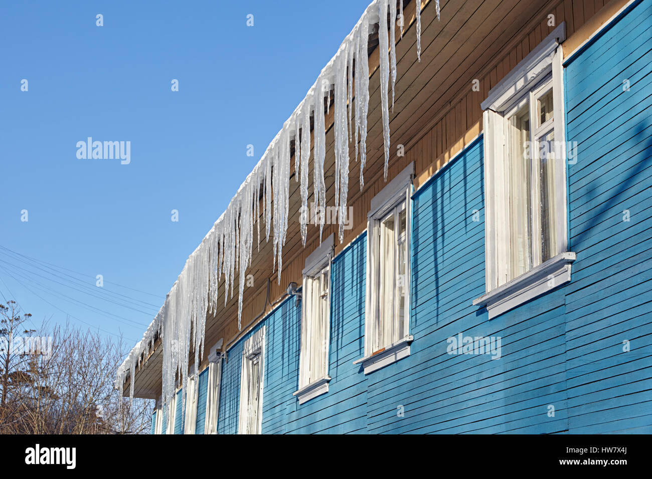 Dangerous icicles hanging from the roof of a wooden house Stock Photo