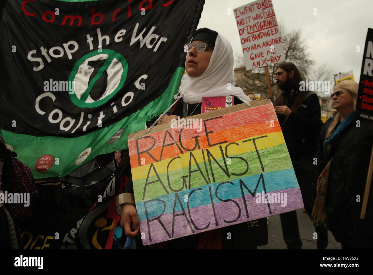 London, UK, 18th March 2017. Campaign group Stand Up to Racism holds a march through central London to mark UN anti-racism day. A woman holds a Stop the War banner and a placard saying 'Rage Against Racism'. Roland Ravenhill/ Alamy Live News Stock Photo