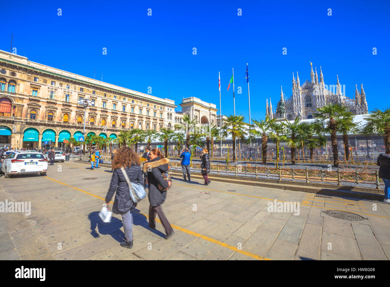 Milan, Italy - March 7, 2017: Famous Milan Dome Cathedral, the Duomo in a blue sky day. Tourists and new palm and banana trees planted in front square Stock Photo