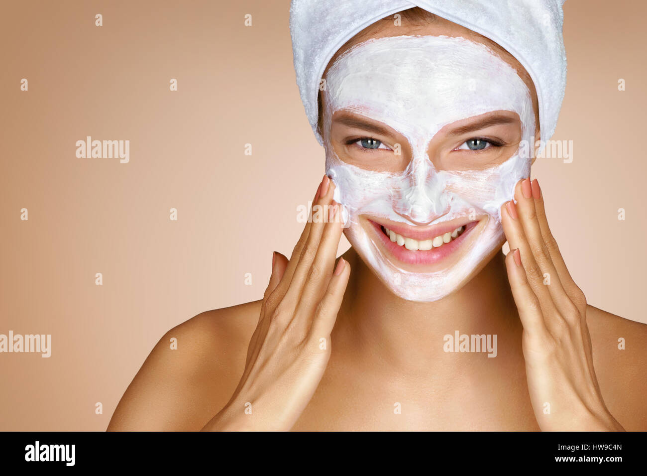 Beautiful woman applying cosmetic cream on her face. Close up of woman on beige background. Skin care concept Stock Photo