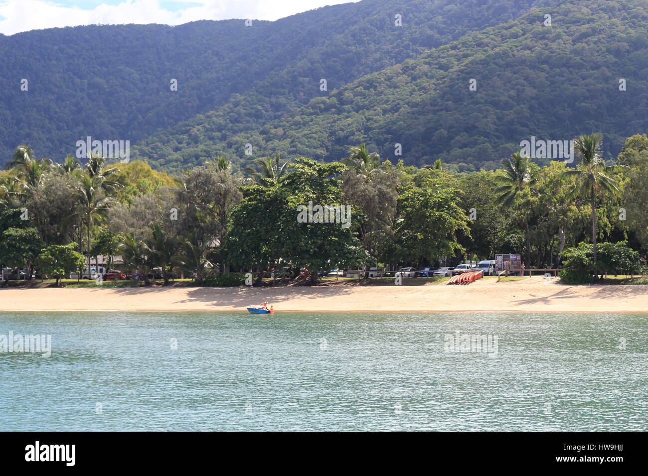 Palm Cove beach at the northern end with tree covered esplanade and the rainforest covered hills seemingly close behind Stock Photo