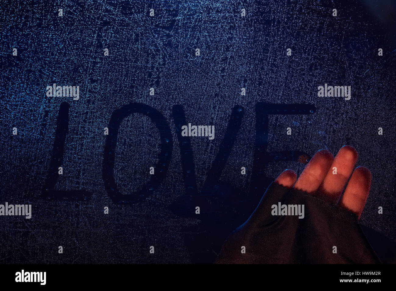 Hand removing love word from frozen window glass background. Wiping out