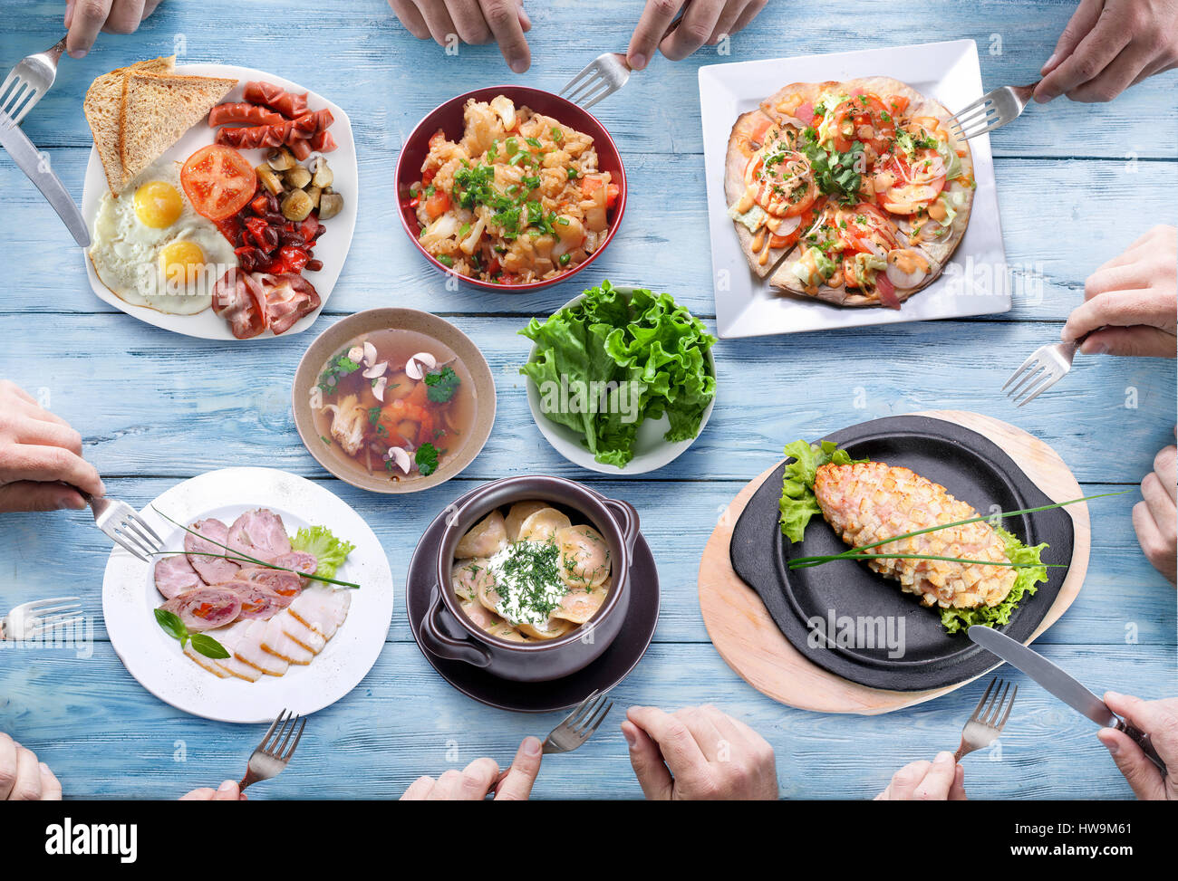 Table covered with different meals and people hands. Stock Photo