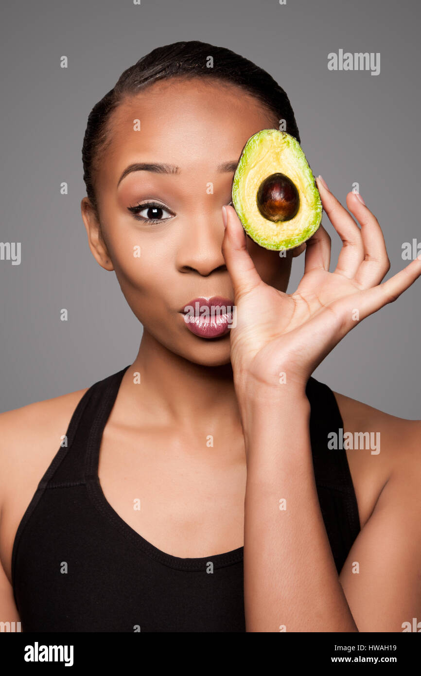 Beautiful healthy happy black asian woman holding delicious avocado super fruit in front of eye. Stock Photo