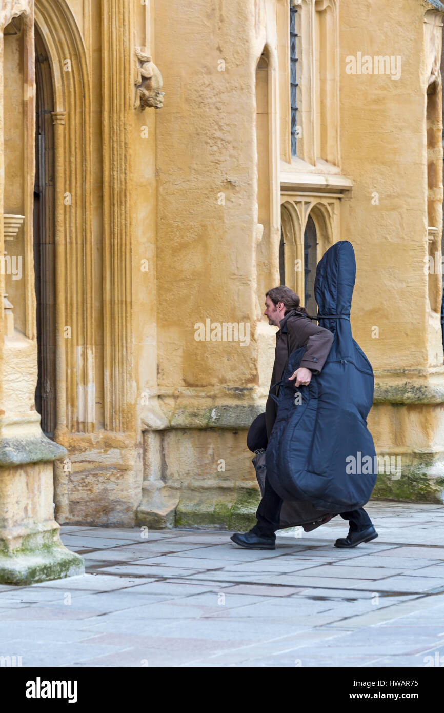 Cirencester - Man carrying double bass musical instrument entering St John the Baptist Church at Cirencester, Gloucestershire in March Stock Photo