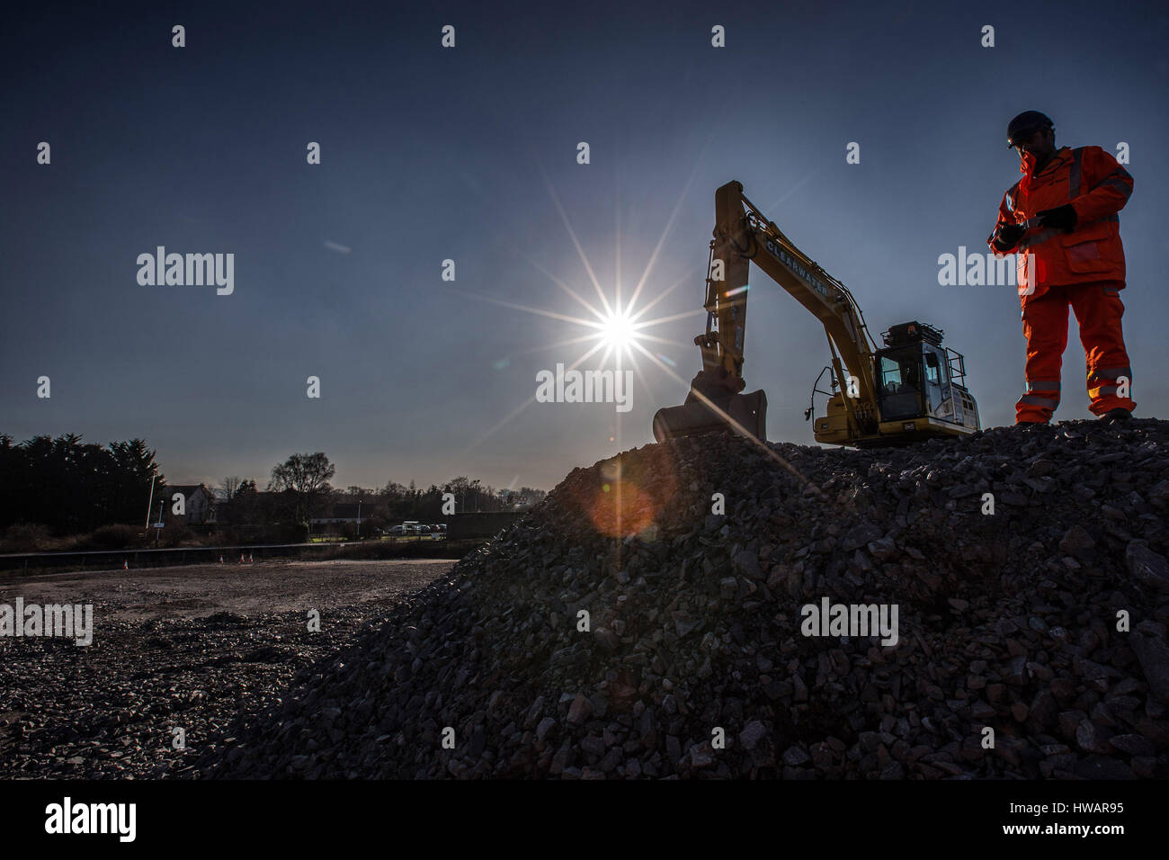 Construction Worker sillhouetted with digger in background Stock Photo