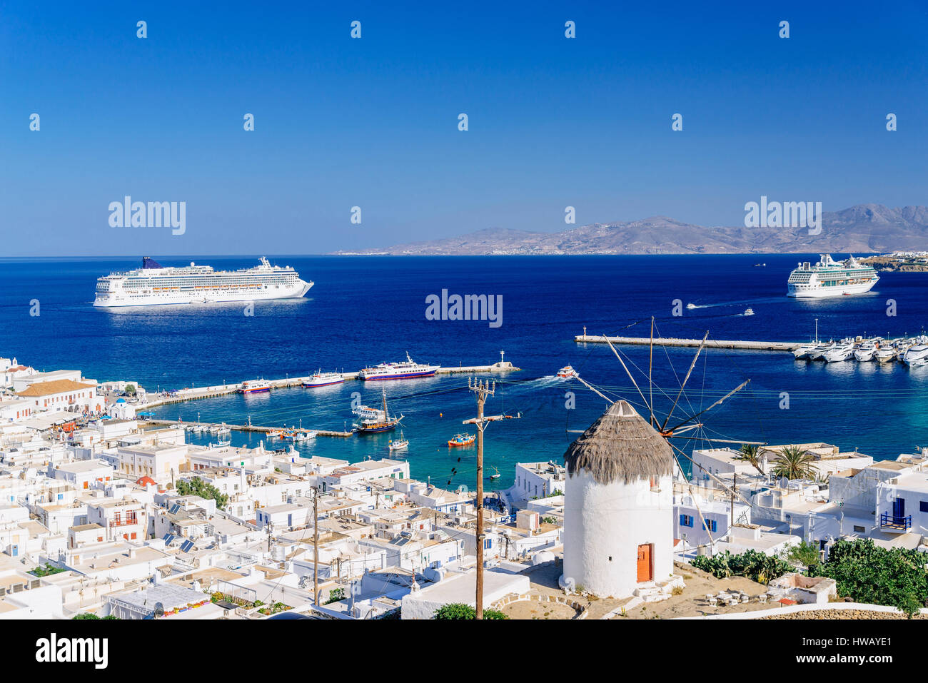Whitewashed city of Mykonos and a famous greek windmill with cruise ships in the distance, Mykonos island, Cyclades archipelago, Greece Stock Photo