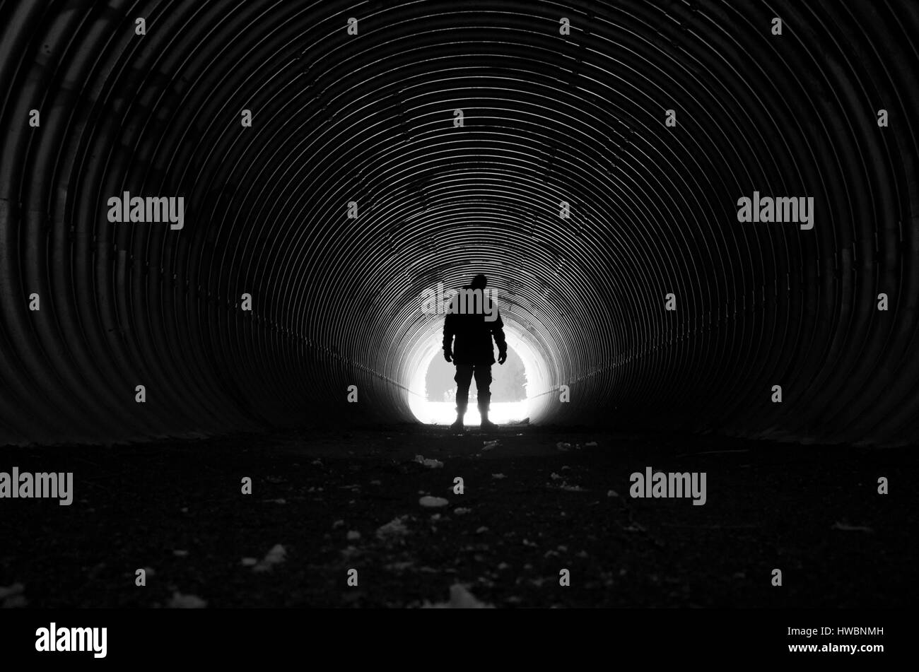 Human standing in dark tunnel with light at other end. Beautiful, mystical and poetic black and white photo. Calm and peaceful mood. Stock Photo