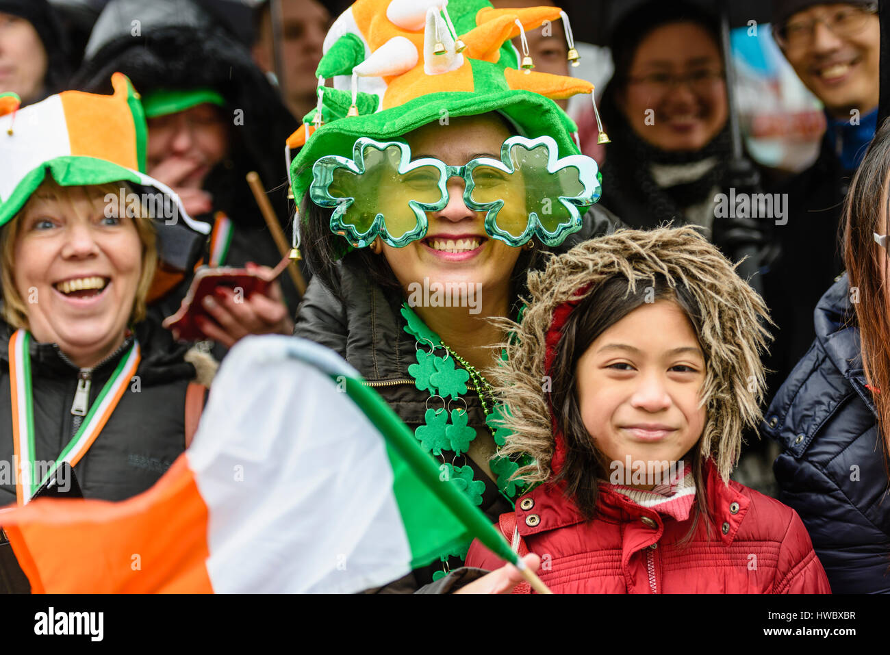 Belfast, Northern Ireland. 17 Mar 2016 - Tourists wear green, white and yellow hats, shamrocks and wave an Irish tricolour flag to celebrate Saint Patrick's Day. Stock Photo