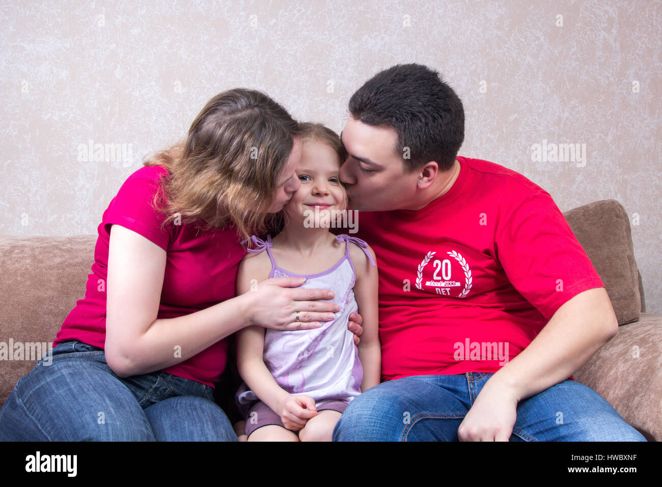 Mom and Dad kiss their daughter on the couch Stock Photo. 