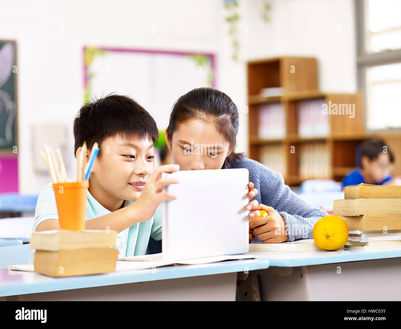 asian elementary schoolgirl and school boy using tablet computer together in classroom. Stock Photo