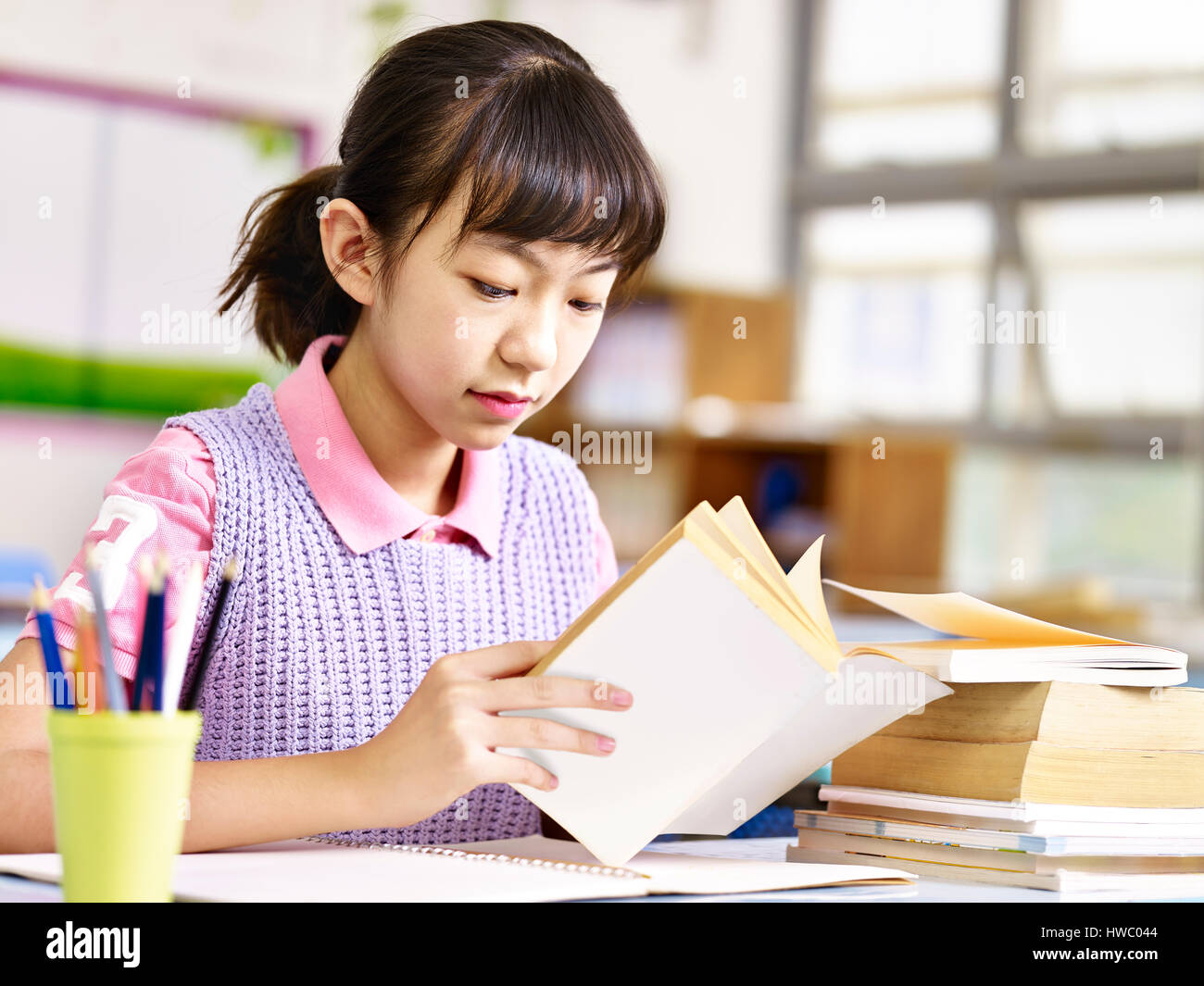 asian primary school pupil reading a book in classroom. Stock Photo
