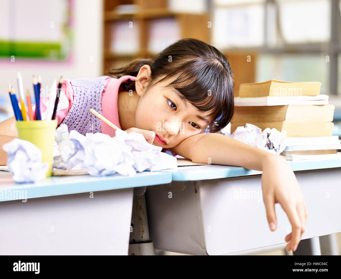 asian elementary school girl frustrated after several failed attempts while writing an essay. Stock Photo