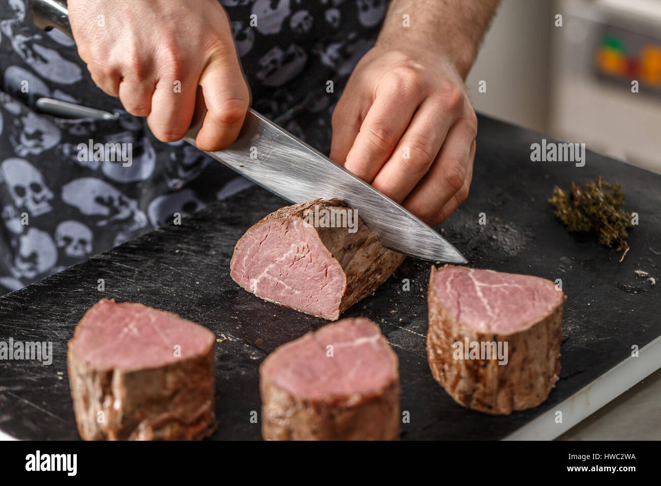 Chef is cutting boiled beef meat on black chopping board Stock Photo