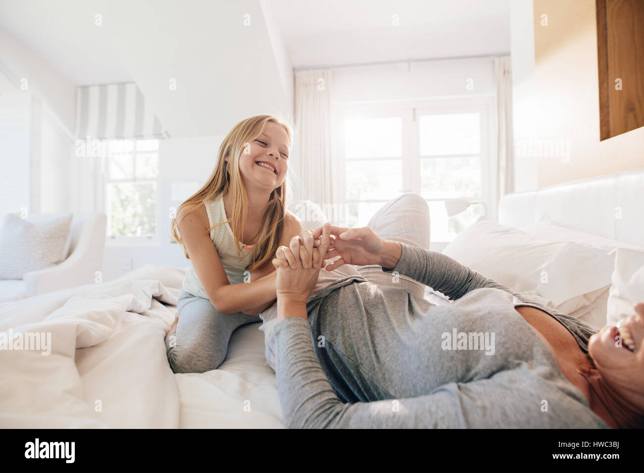 Happy little girl with her mother on bed. Mother and daughter playing in bedroom. Stock Photo