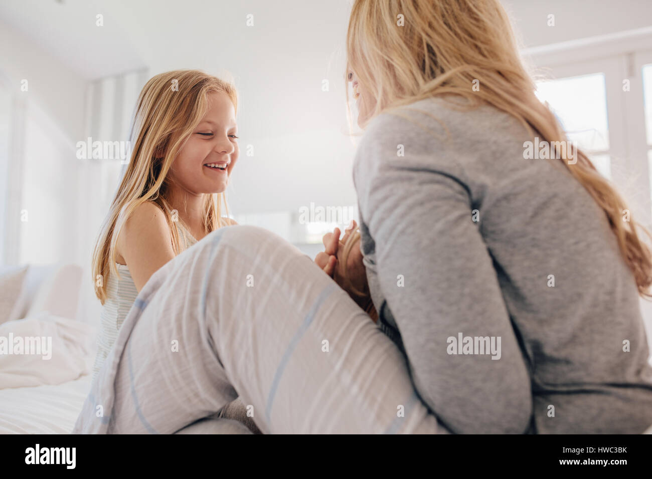 Happy little girl on bed playing with her mother. Cute young family playing in bedroom. Stock Photo