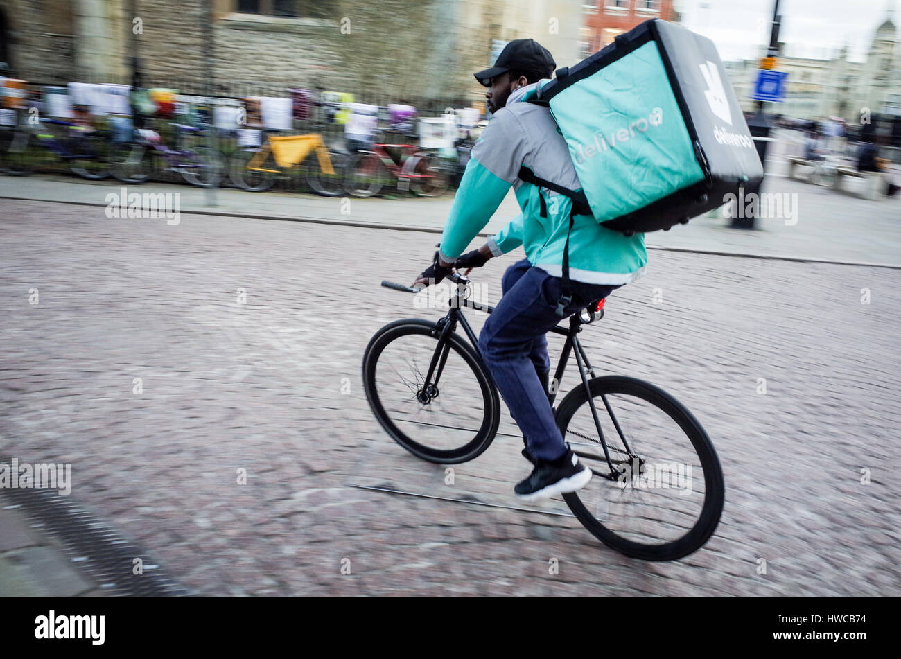 A Deliveroo food courier rushes through the streets of central Cambridge Stock Photo