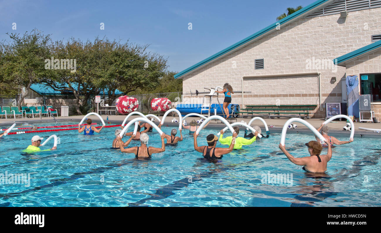 Group of women, 1 man, including seniors, attending Water Aerobics class, instructor demonstrating,  using  styrofoam 'water noodle'. Stock Photo