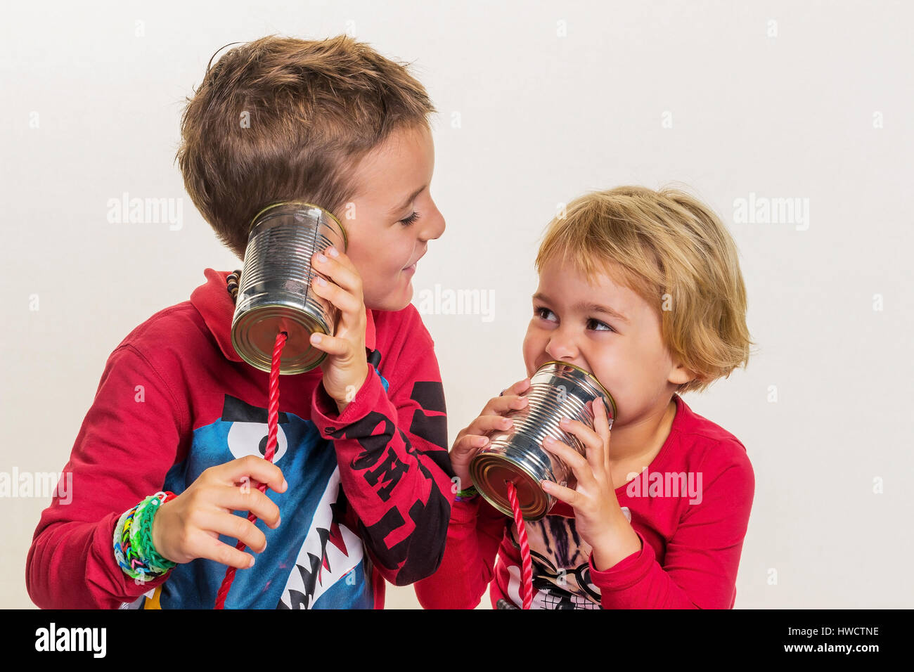 Two small children call up a phone from two tins., Zwei kleine Kinder telefonieren mit einem Telefon aus zwei Dosen. Stock Photo