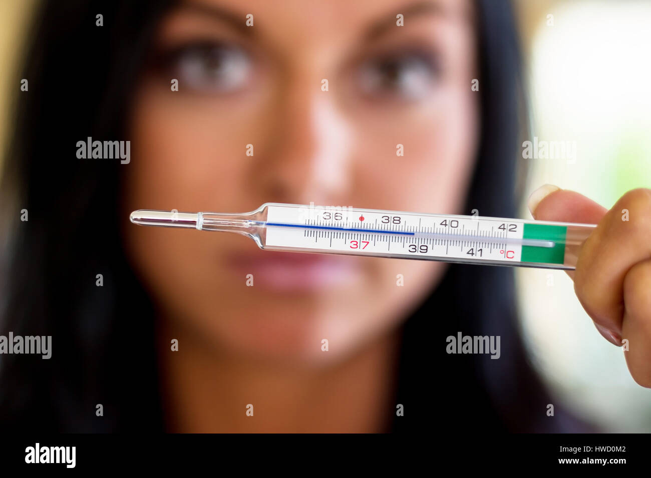 A woman holds a clinical thermometer Hinterhand. Symbolic photo for ill