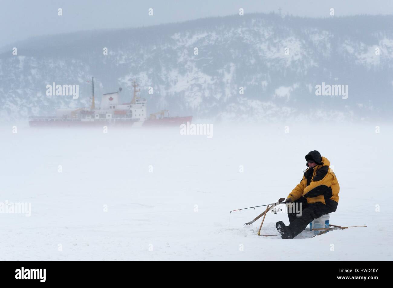 Canada, Quebec, Saguenay, La Baie, white fishing village of Anse a Benjamin, one man fishing on the ice, icebreaker in the background Stock Photo