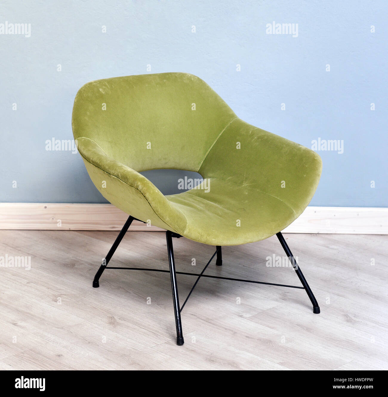Furniture Still Life of Small Retro Green Velvet Plush Reclining Chair with Black Metal Legs in Room with Wood Floor and Light Blue Wall Stock Photo