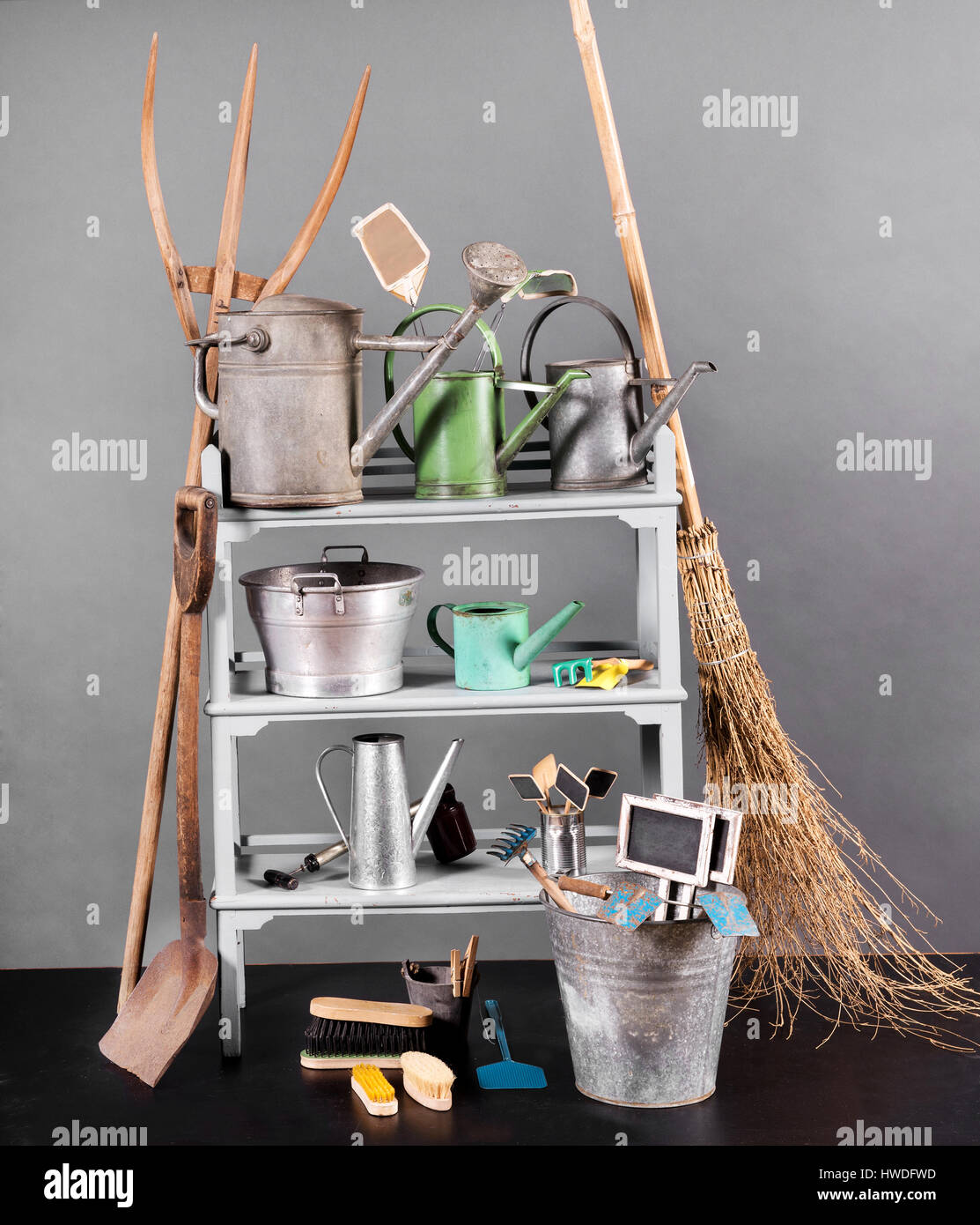 Assortment of vintage gardening tools arranged on shelves with watering cans, bucket, straw broom, spade and fork with plant labels and accessories Stock Photo
