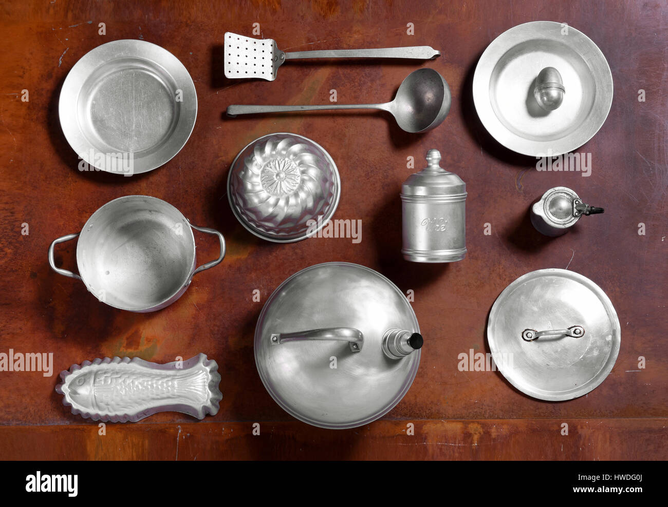 Still life arrangement of aluminium kitchen tools on a wooden table with moulds, kettle, plate, saucepan, lid, dish and cooking utensils in an overhea Stock Photo