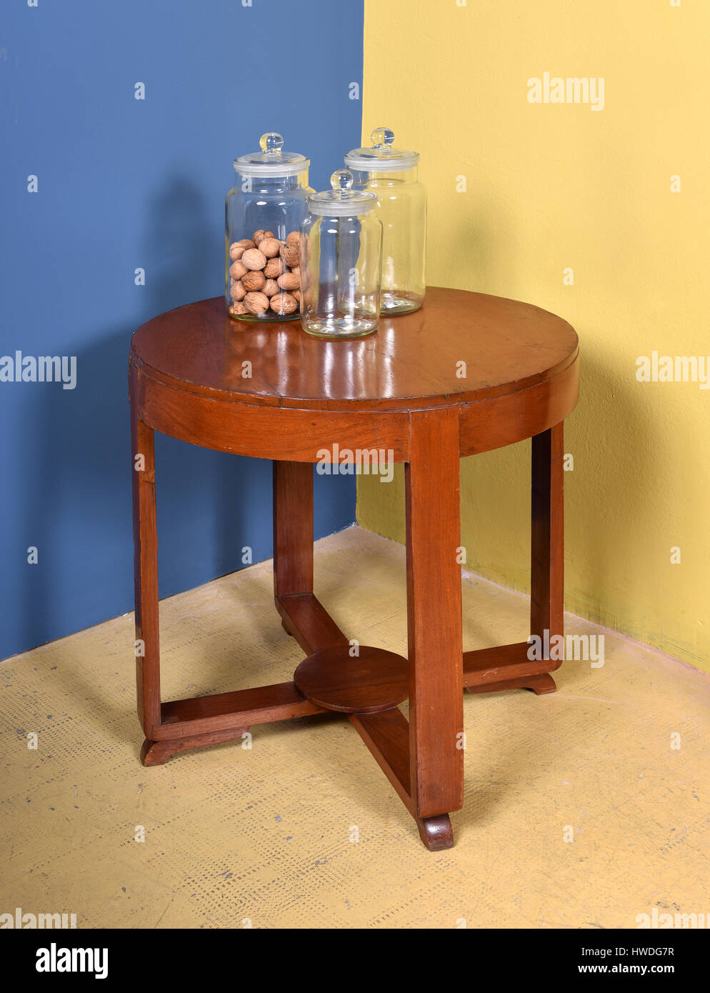 Retro Furniture Still Life of Small Round Wood Side Table with Collection of Three Glass Jars - One with Nuts - in Room with Blue and Yellow Walls Stock Photo
