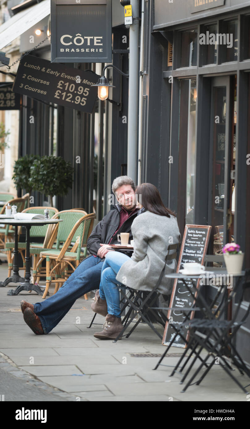 A man and woman sit at a cafe talking along Black Jack Street, Cirencester in the Cotswolds, Gloucester, England, UK Stock Photo