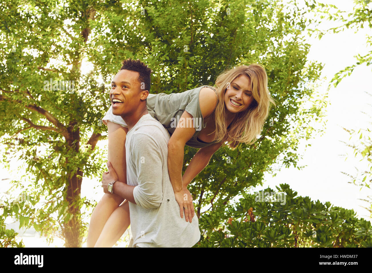 Young man carrying female friend over his shoulder in park Stock Photo