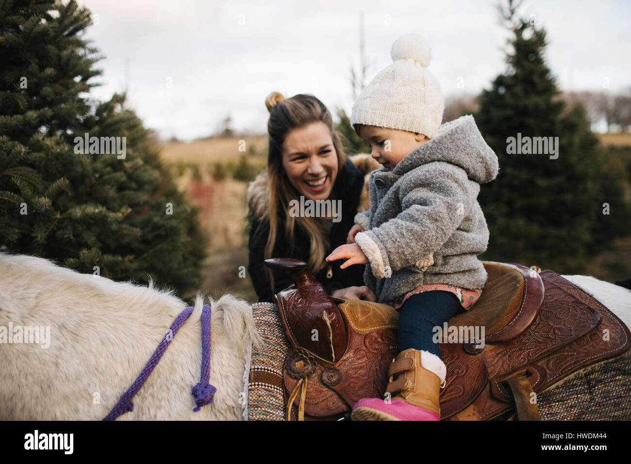 Mother smiling at baby girl riding on horse Stock Photo