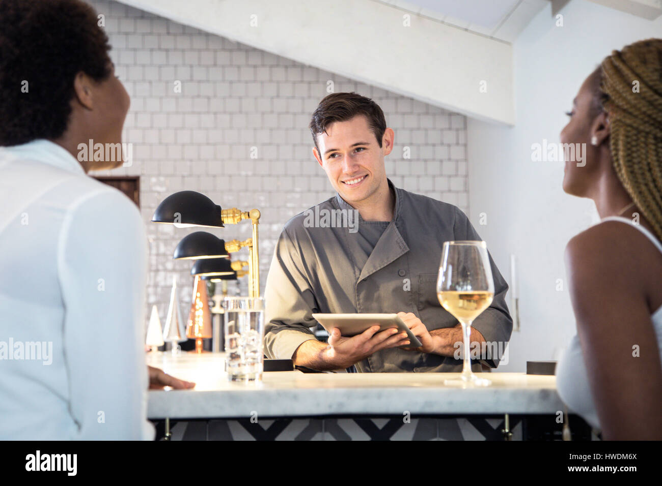 Barman serving customers at bar, barman using digital tablet Stock Photo