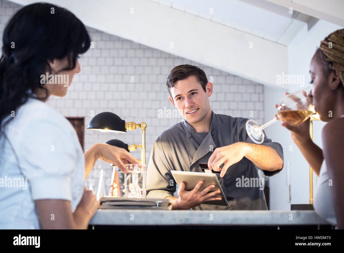 Barman serving customers at bar, barman using digital tablet to take payment Stock Photo
