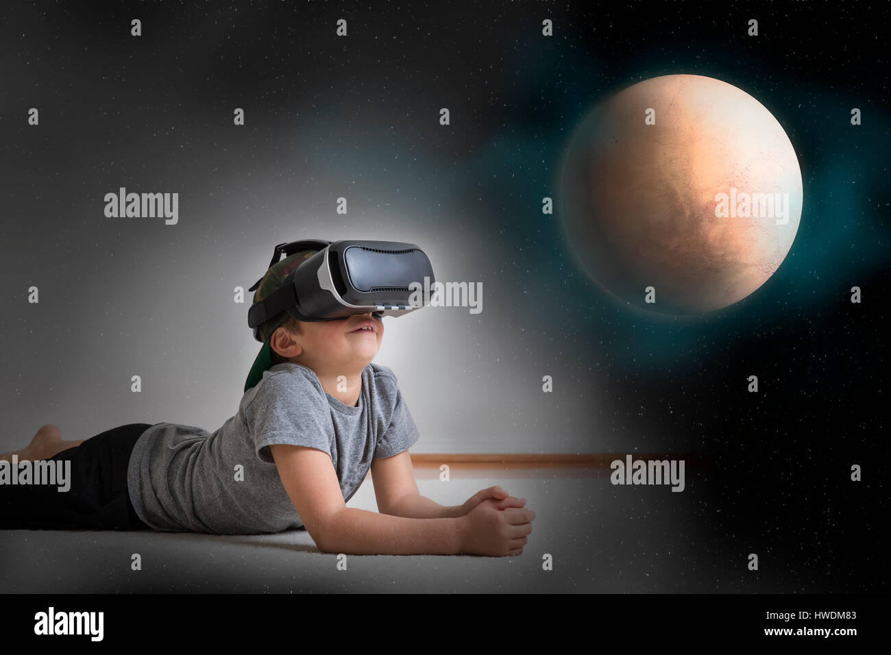 Young boy lying on floor, wearing virtual reality headset, looking at planet, digital composite Stock Photo