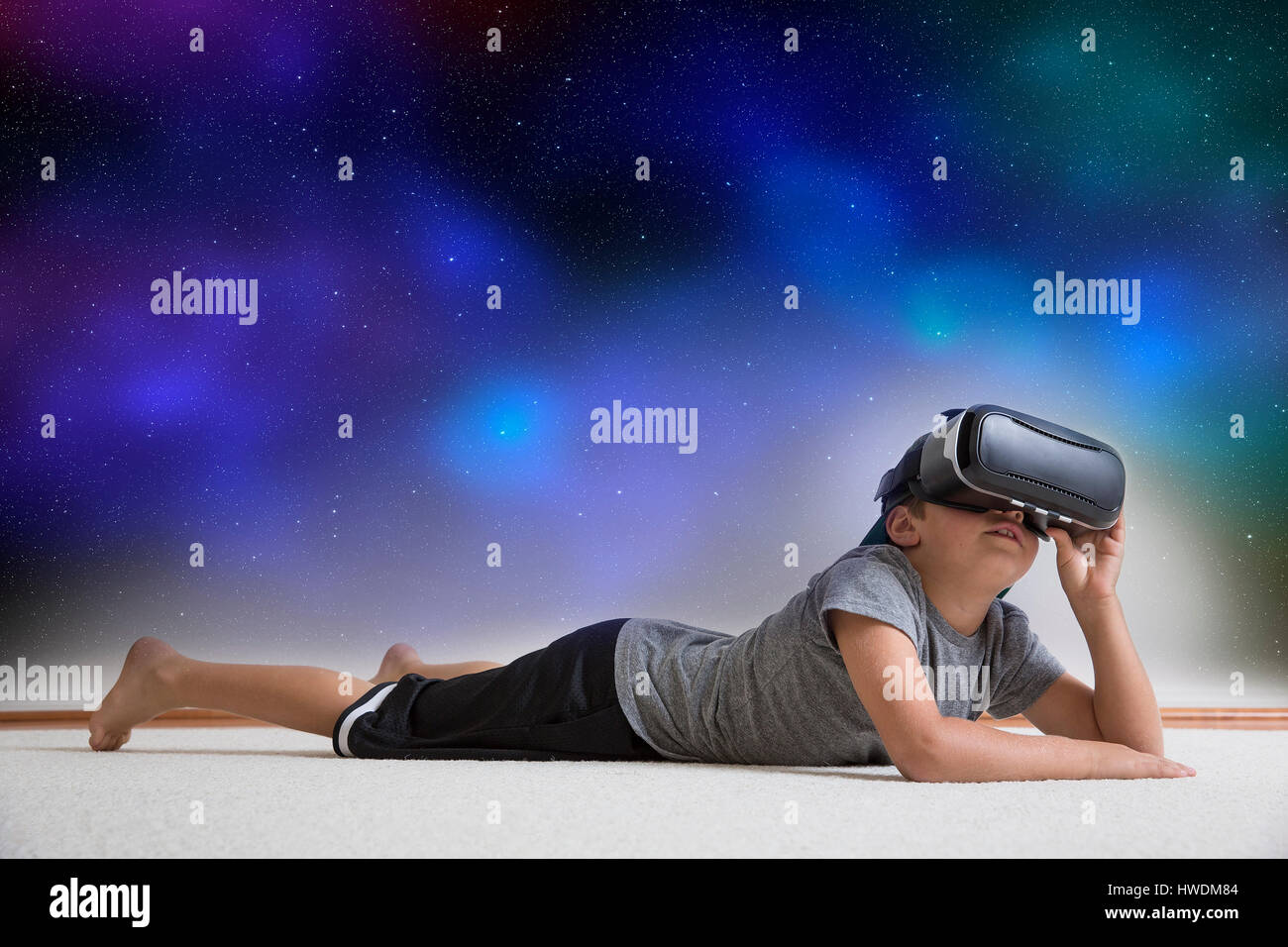 Young boy lying on floor, wearing virtual reality headset, looking into night sky, digital composite Stock Photo