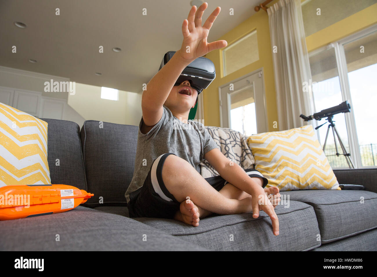 Young boy sitting cross legged on sofa, wearing virtual reality headset,  hands reaching out in front of him Stock Photo - Alamy