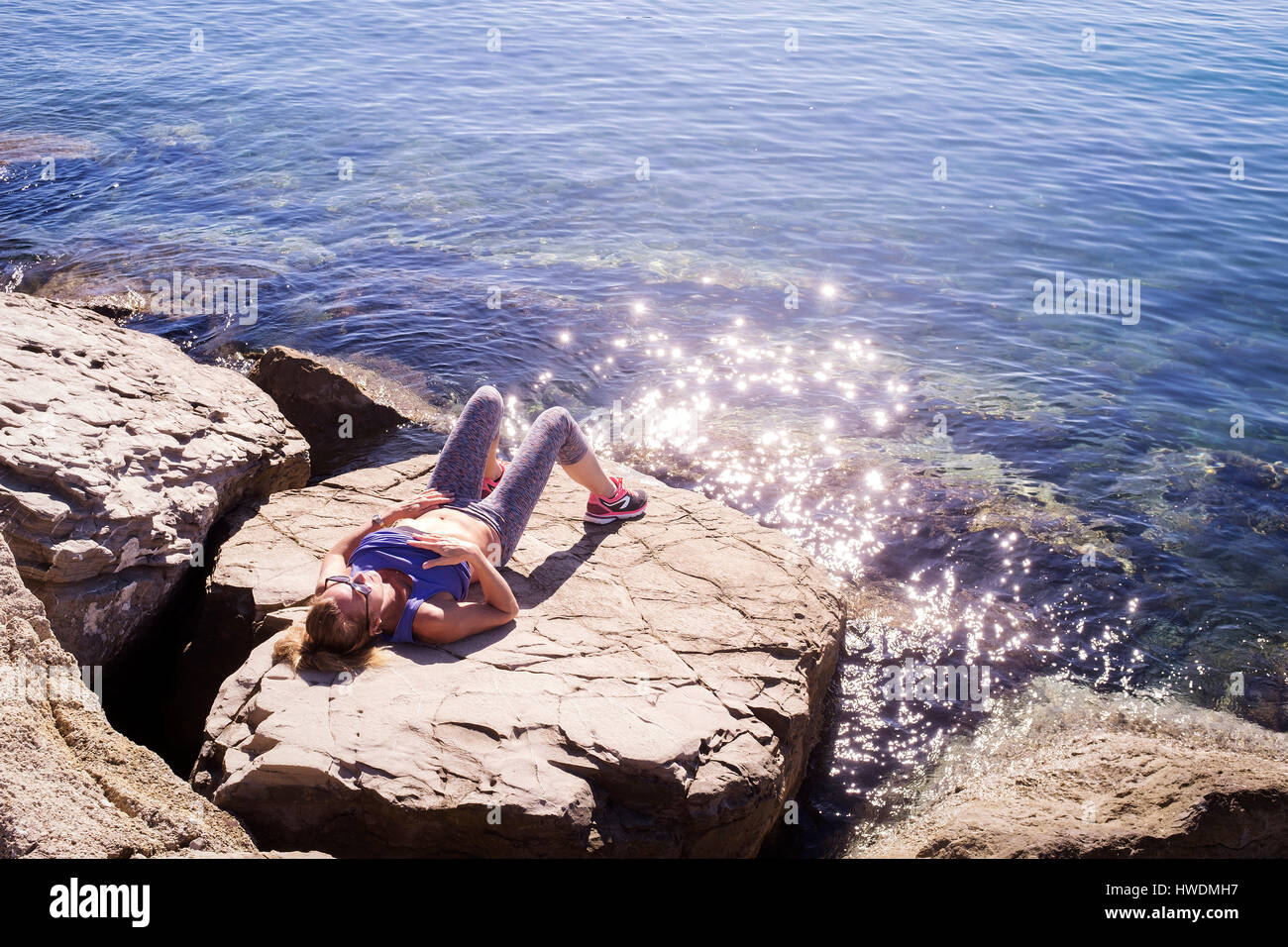 Woman sunbathing on rocks by sea Stock Photo
