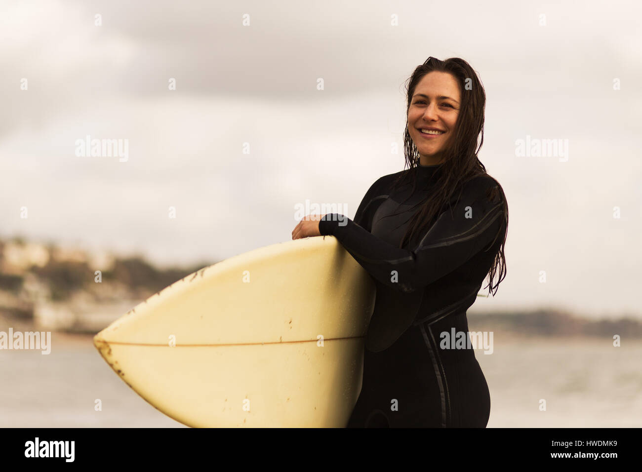 Young woman walking away from sea, carrying surfboards Stock Photo