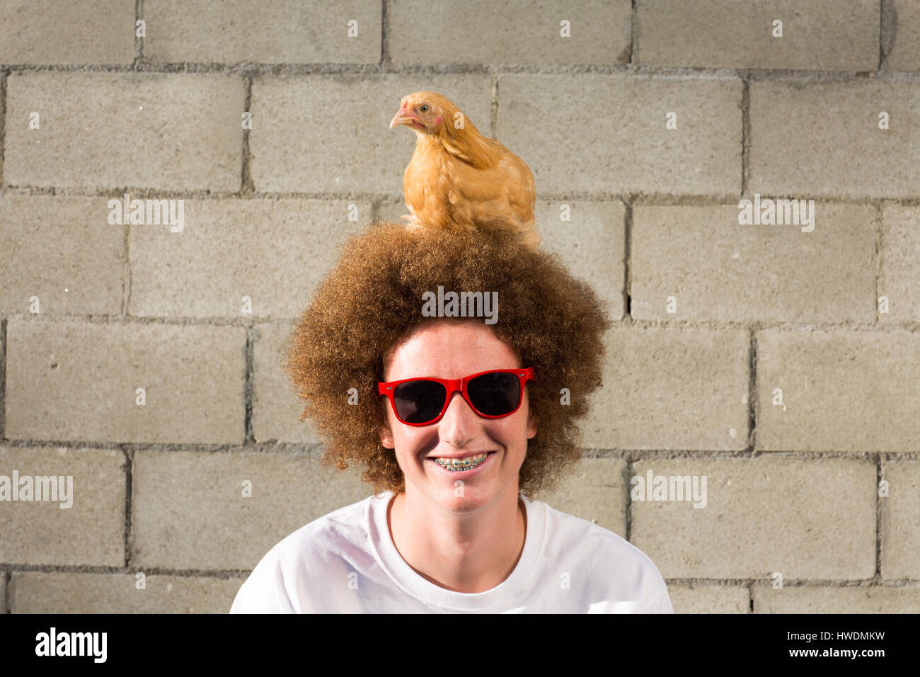 Portrait of teenage boy with red afro hair, chicken sitting on head Stock Photo