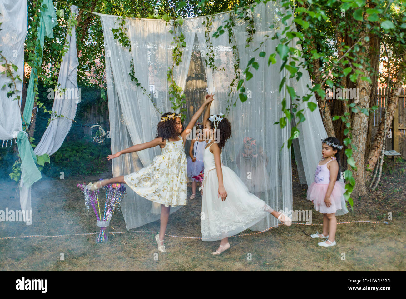 Two young girls, dressed as fairies, dancing outdoors, younger girl watching from side Stock Photo