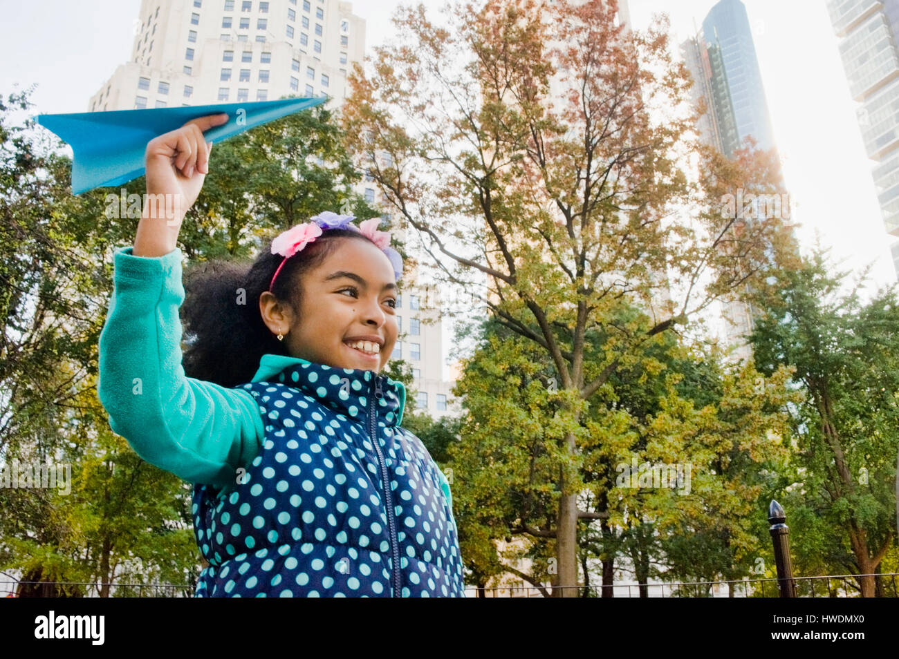 Girl throwing paper airplane smiling, New York, USA Stock Photo
