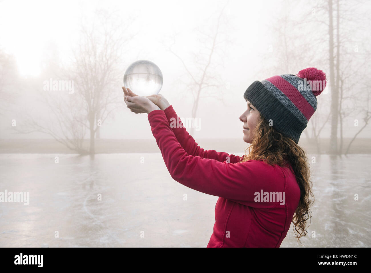 Woman holding up crystal ball on frozen lake Stock Photo