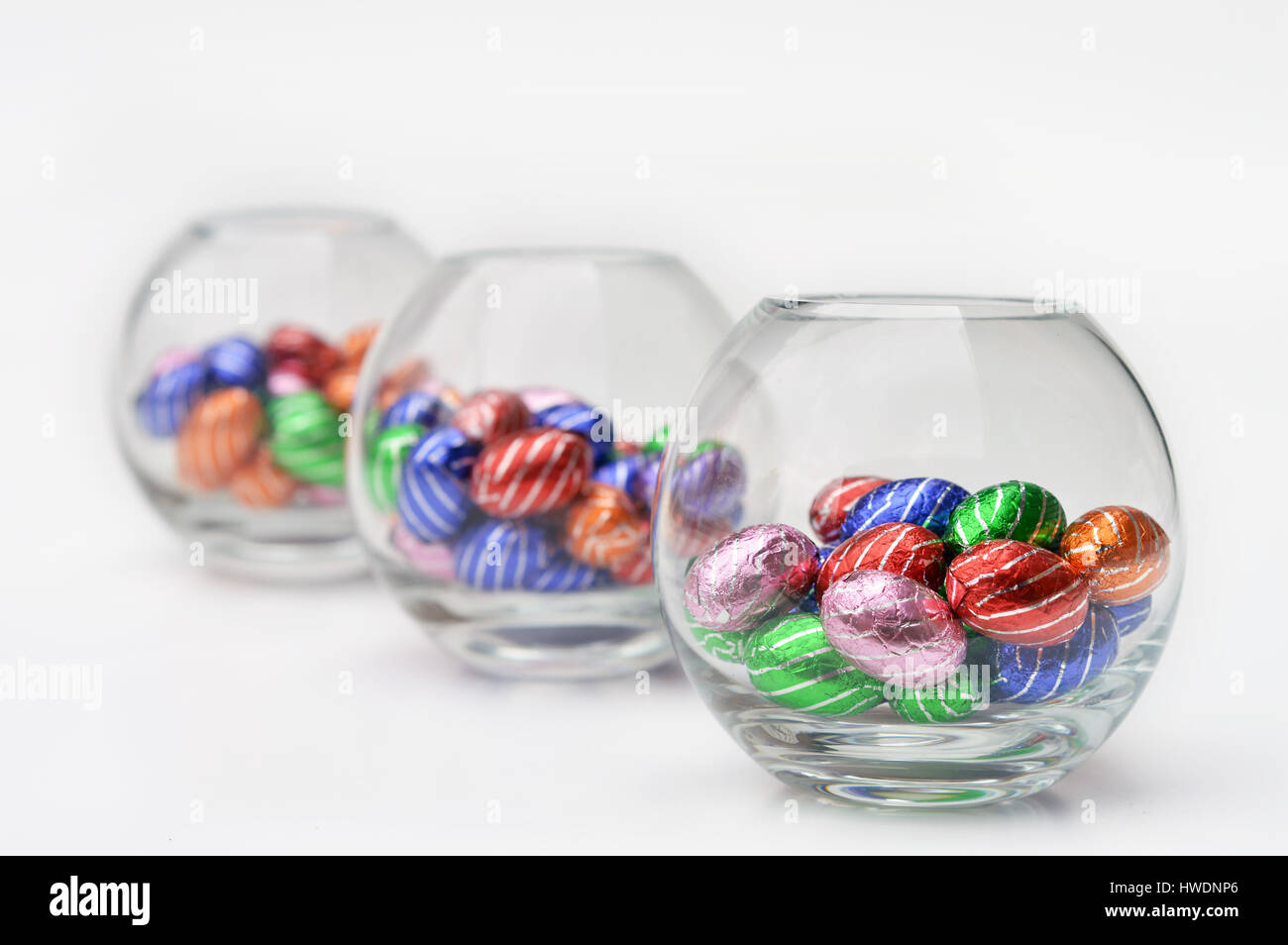 3 Glass spheres filled with chocolate easter-eggs, on white with focus on the first bowl Stock Photo