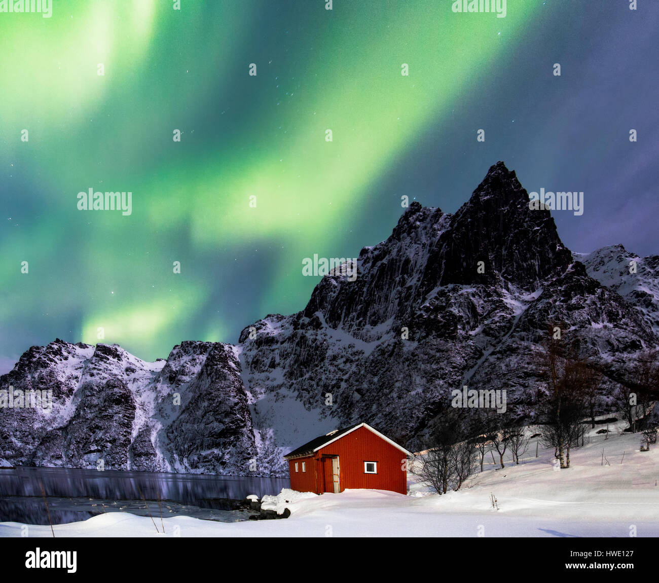 Lofoten, Svoelver, Aurora Borealis over a frozen lake and red rorbu, Norway. Stock Photo