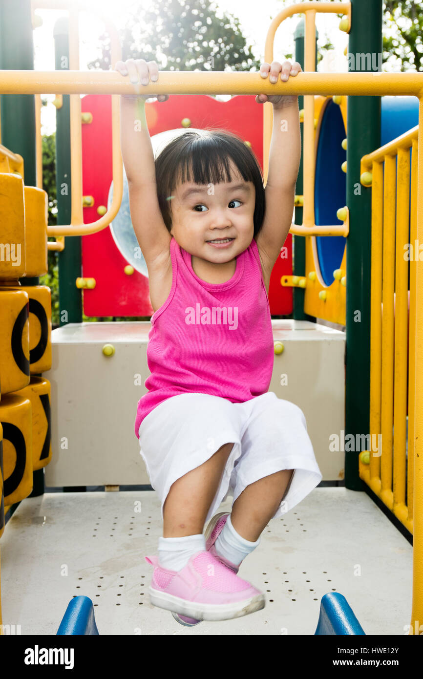 Asian little Chinese girl hanging on horizontal monkey bar at the playground during the summer