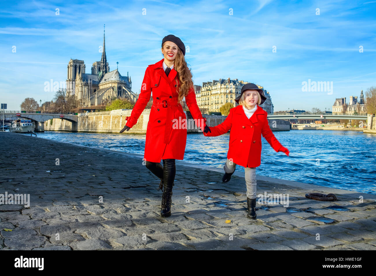 Bright in Paris. Full length portrait of trendy mother and daughter tourists in red coats on embankment in Paris, France having fun time Stock Photo