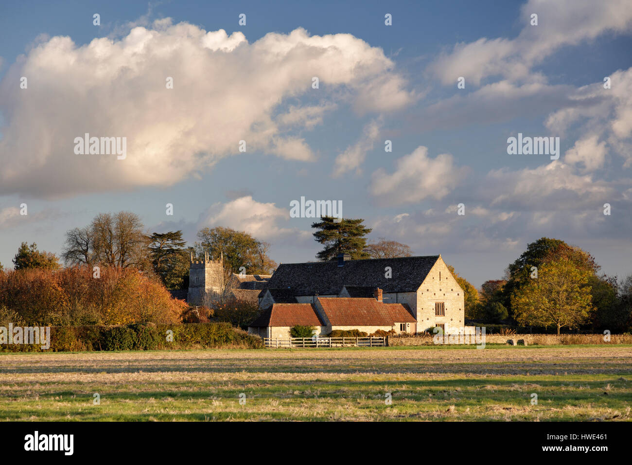 View across farmland towards the village of Somerford Keynes in Gloucestershire with converted barns and a church tower Stock Photo