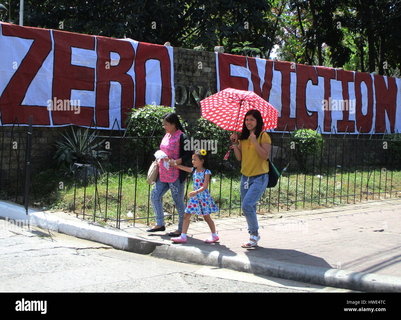 Filipinos walk past a banner unfurled by protesters outside the National Housing Authority in Quezon City, Philippines on Monday, March 20, 2017, during a rally against a planned serving of an eviction notice to occupiers of a vacant housing project in Bulacan province. An urban poor group organized an occupation of several vacant government housing projects in Bulacan province on March 8, 2017 to protest the Philippine government's alleged failure to provide housing to its people, with authorities warning the group and its members to voluntarily go away, or face a forceful eviction. (Photo by Stock Photo