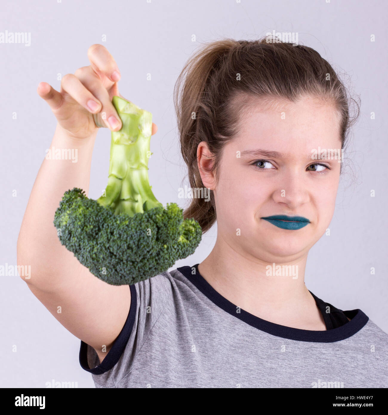 A pretty girl skeptically holds a broccoli in her hand Stock Photo